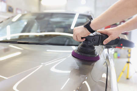 Man with an orbital polisher in car workshop polishing car closeup