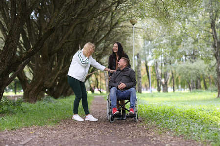 Man in wheelchair and laughing female friends walking in parkの写真素材