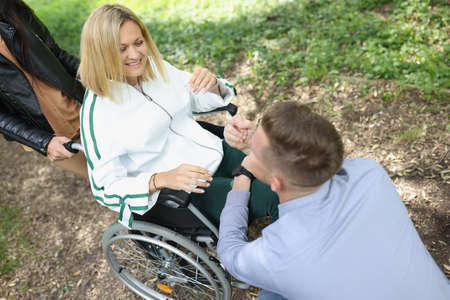 Man communicates with smiling disabled woman in chair in park
