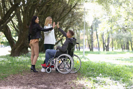 Disabled man in wheelchair giving five to female friends in parkの写真素材