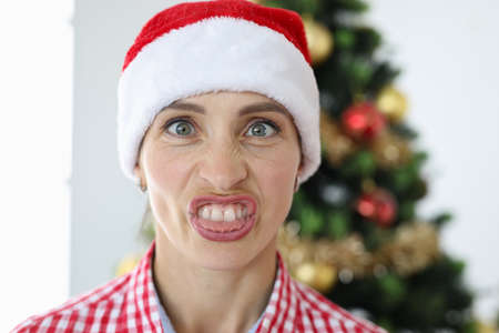 Portrait of irritated woman in santa claus hat on background of christmas tree