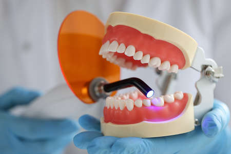 Doctor holds jaw and dental UV lamp to fill dental jaw