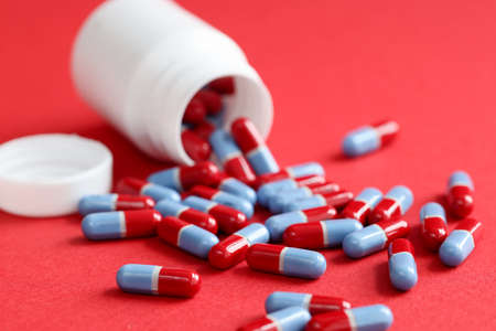 Blue-red medical pills scattered from jar lie on a red backgroundの写真素材