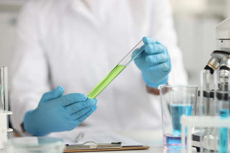 Scientist in protective gloves holds test tube with green liquid closeup