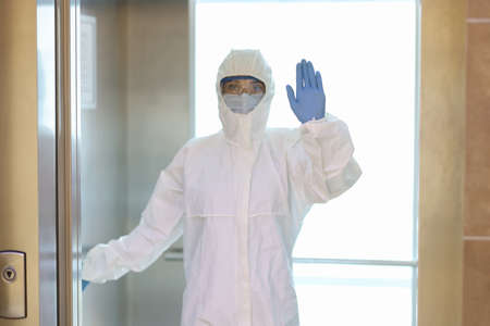 Woman in protective suit and medical mask with gloves stands in elevator