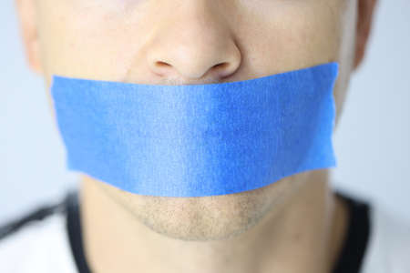 Portrait of woman with mouth sealed with blue tapeの写真素材