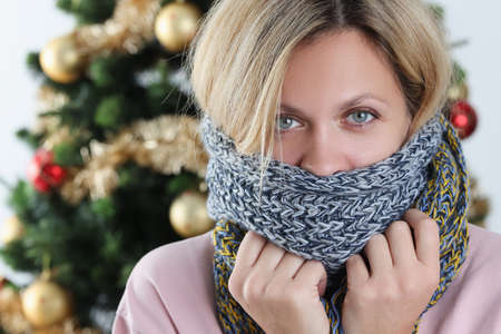 Portrait of young woman wrapped in scarf on background of Christmas treeの写真素材