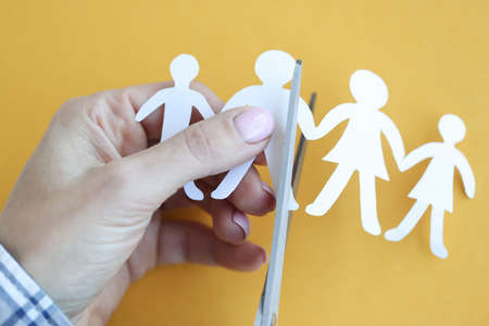 Woman hand cuts paper figures in form of family with scissors closeup