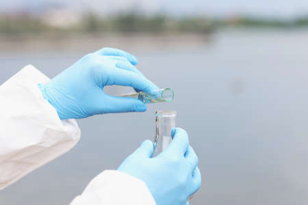 Scientist in gloves and protective suit pours dirty water from test tube into flaskの写真素材
