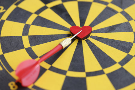 Red small wooden heart in center of dart board and dart closeup
