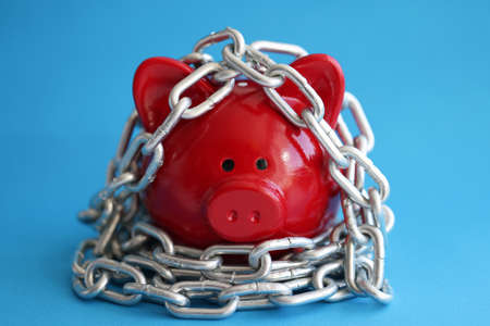 Red pig piggy bank is wrapped in chrome chain closeupの写真素材