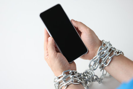 Hands wrapped in chain hold black smartphone closeupの写真素材