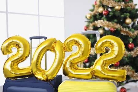 Golden helium balloons with numbers 2022 standing on suitcases Christmas tree closeup