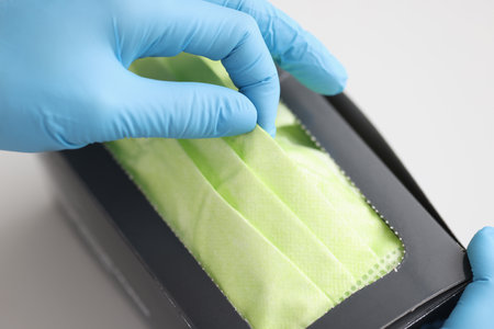 Rubber gloved hand pulling protective medical face mask out of box closeupの写真素材