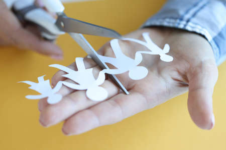 Woman cuts paper figures of family with scissors closeup