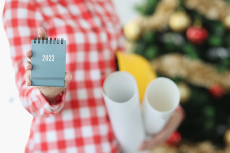 Woman hand holds calendar for 2022 and hard hat with paper rollの写真素材