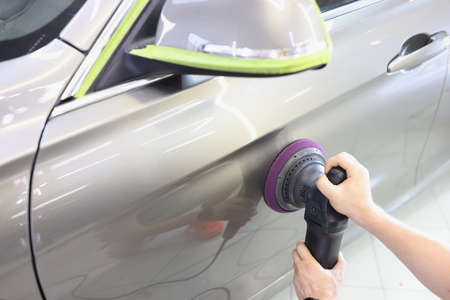 Mechanic polishing door of car with grinder closeup