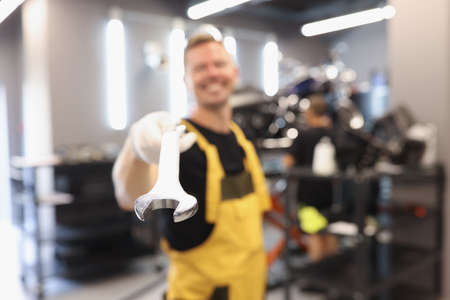 Uniformed car repairman holds wrench in car repair shop