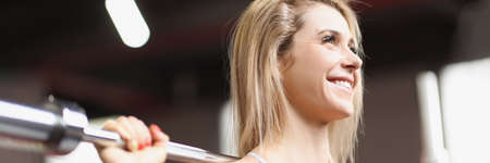 Portrait of smiling woman doing exercises with heavy barbell