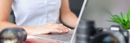 Woman typing on laptop keyboard at table with camera lenses closeupの写真素材