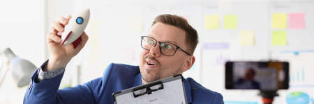 Emotional male blogger holds rocket in hand and conducts online training on quick start in business