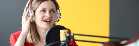 Woman singer in headphones singing song into microphone in recording studioの写真素材