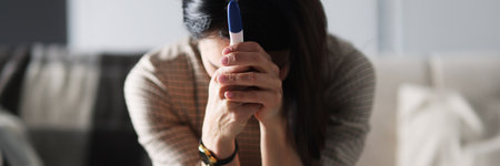 Upset woman is sitting on couch and holding pregnancy testの写真素材