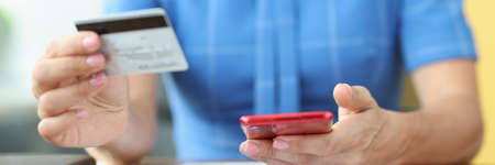 Woman sitting at table with documents and holding mobile phone and credit bank card in her hands closeupの写真素材
