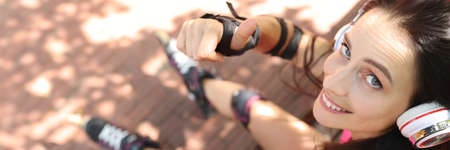 Young woman in roller skates sitting on asphalt and showing thumb upの写真素材