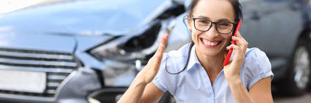 Satisfied woman talking on mobile phone near wrecked carの写真素材