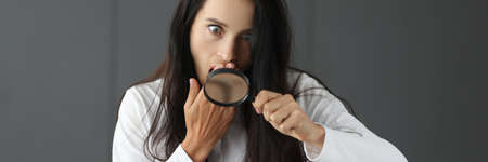 Surprised woman looking through magnifying glass and covering mouth with hand