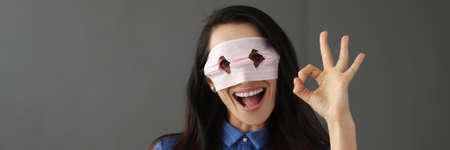 Young woman looking through holes on medical protective mask and showing hand ok gesture