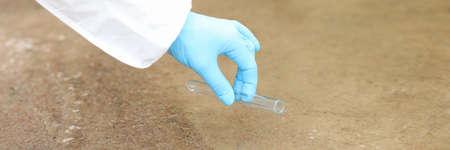 Gloved scientist takes water samples into test tube from lake closeup