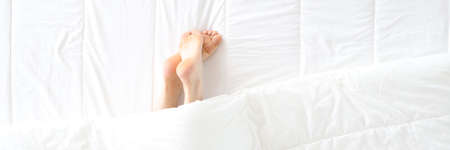 Women legs stick out from under covers in bedの写真素材