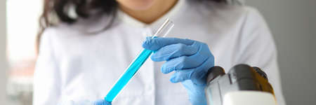 Scientist hands in gloves holds test tube with blue liquid in laboratory