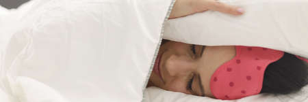 Woman lies in bed covering head with blanket closeup