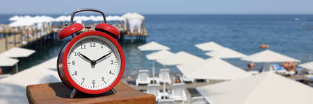 Red alarm clock stands against background of the beach and seaの写真素材