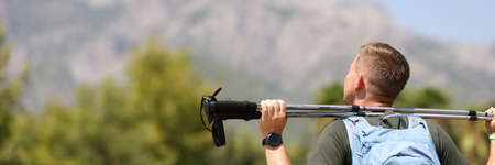 Young man stands on top of mountain and holds Nordic walking sticks