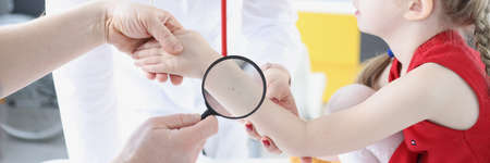 Doctor examining baby skin on hand with magnifying glass in clinicの写真素材