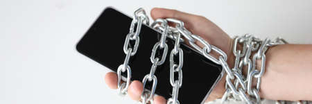 Male hands tied with chain and hold smartphoneの写真素材