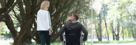 Man in wheelchair is walking in park with his girlfriend