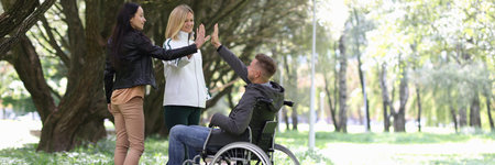 Disabled man in wheelchair giving five to female friends in parkの写真素材