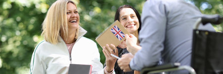 Disabled man in wheelchair giving english textbook to his female friends in park