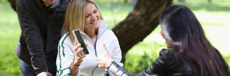 Disabled woman in wheelchair shows smartphone with financial indicators of work to friend in park