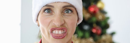 Portrait of irritated woman in santa claus hat on background of christmas treeの写真素材