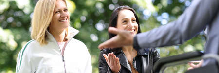 Young women and man in wheelchair laugh and chat in parkの写真素材