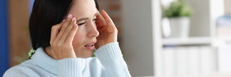 Woman with headache and photophobia looks out window
