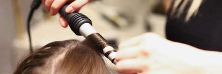 Hairdressers hands doing hair with a curling ironの写真素材