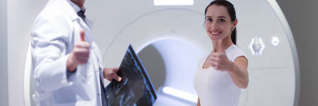 Smiling male doctor and female patient hold thumbs up in office for MRI examination