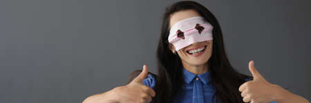 Smiling woman in mask on face holds thumbs upの写真素材